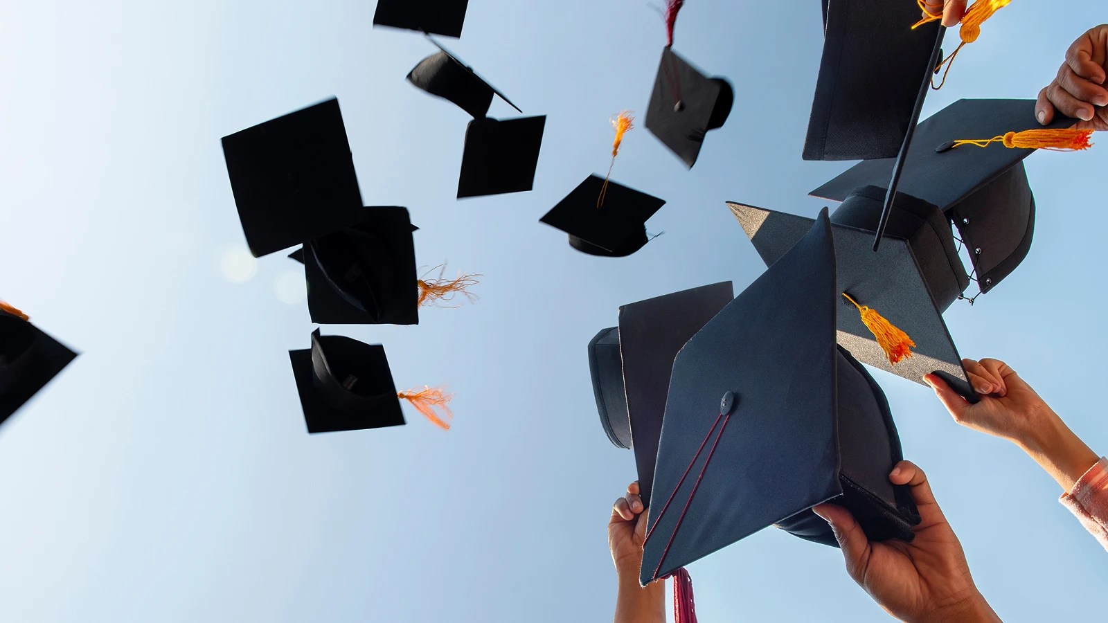 Graduation caps tossed in the air against a clear, blue sky.