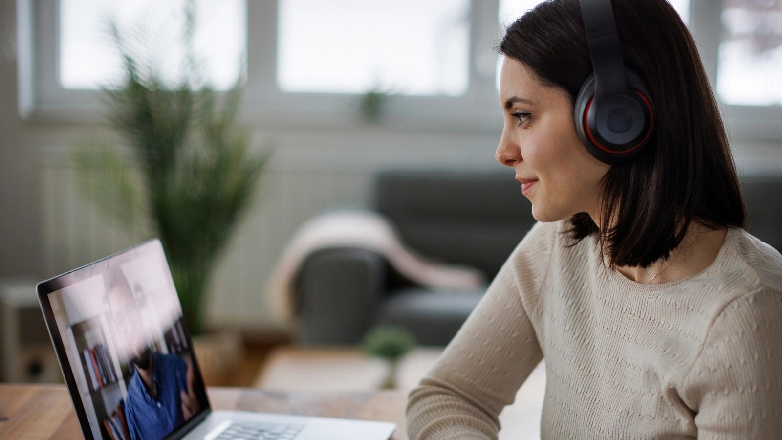 Person wearing headphones on a video call at home, with a cozy background including a sofa and plant.