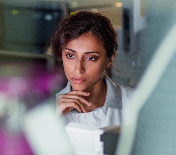 A professional. wearing a lab coat, with dark hair, on their computer, in an indoor setting.
