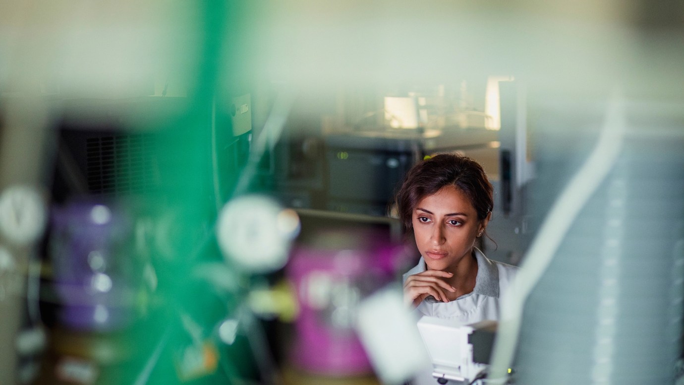 A professional. wearing a lab coat, with dark hair, on their computer, in an indoor setting.