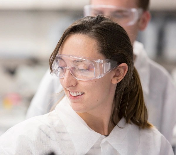 Close-up of individual wearing white lap coat and safety goggles.