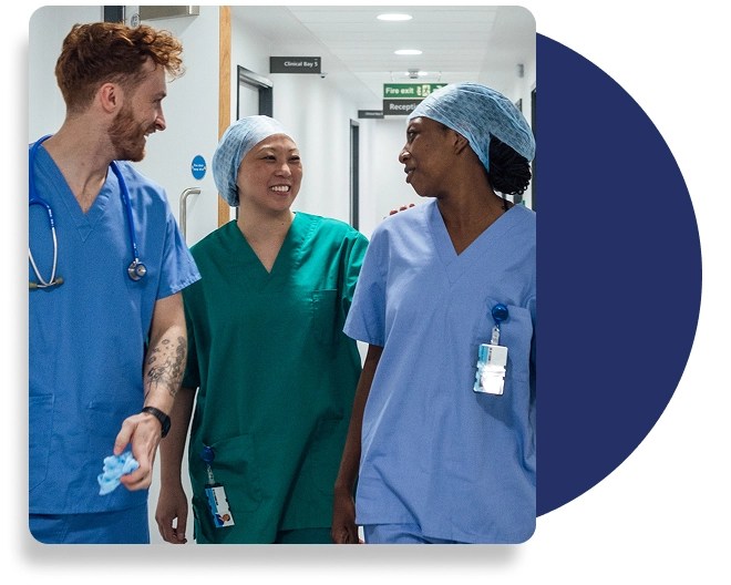 A group of healthcare professionals talk with each other, dressed in scrubs, in a hospital setting.
