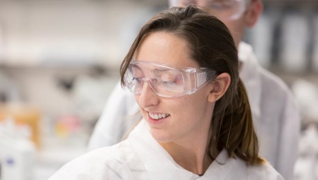 Close-up of individual wearing white lap coat and safety goggles.