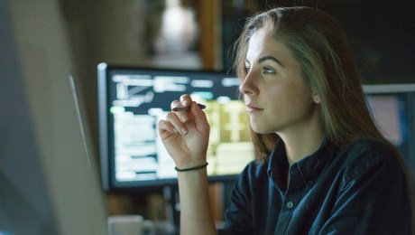 An individual sitting in front a computer, with a computer behind them.