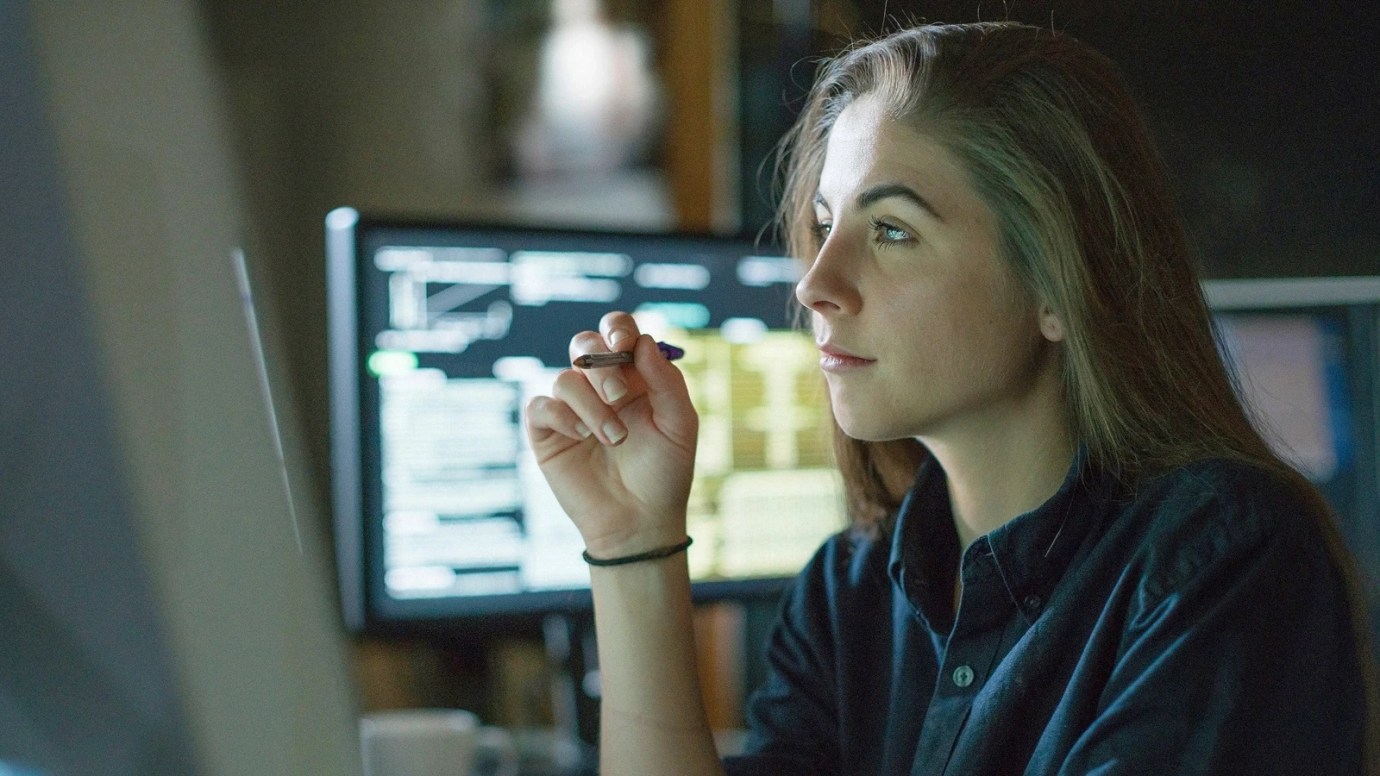 An individual sitting in front a computer, with a computer behind them.