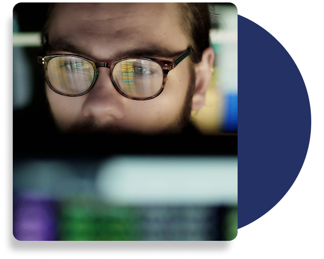 An individual sitting a front of a computer, wearing glasses.
