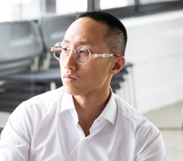 An individual, wearing a white blouse and glasses, sits at their computer working.