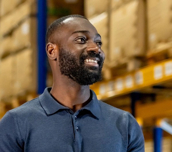 Person holding a tablet and inspecting shelves stacked with cardboard boxes in a brightly lit warehouse.
