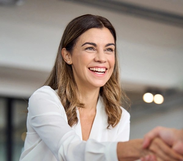 A female professional wearing a white blouse, shakes hands with another individual.