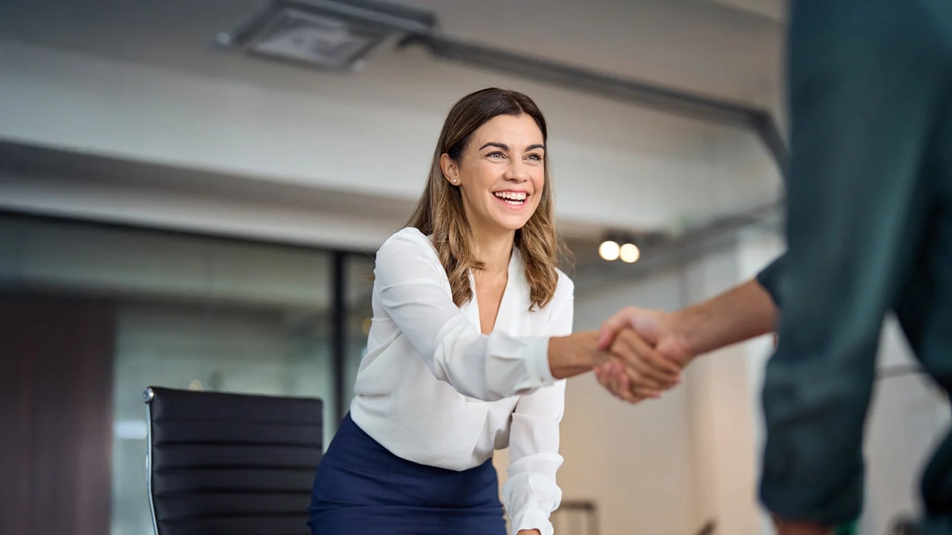 A female professional wearing a white blouse, shakes hands with another individual.