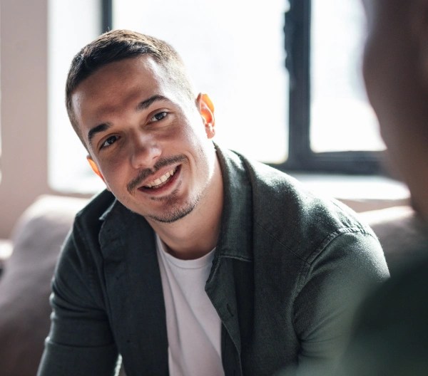 A smiling person displaying their laptop to someone in an indoor setting.