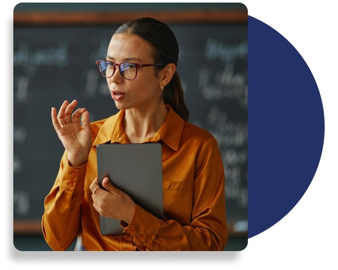 A teacher holding tablet computer addressing students in front of a blackboard.