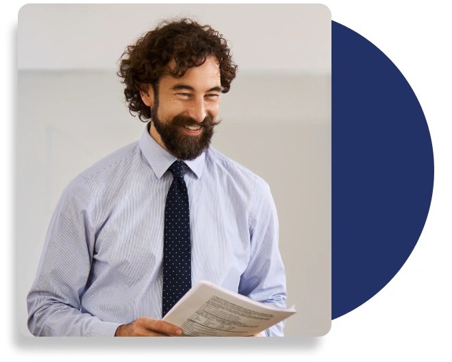 A smartly dressed person with a beard holding a stack of paper.